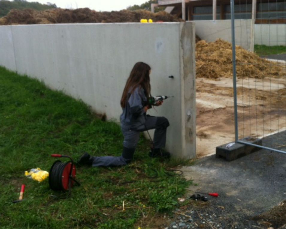Schülerin bohrt mit Bohrmaschine Loch in eine Betonmauer